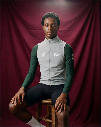 Velodrom model wearing a grey cycling gilet against a burgundy backdrop