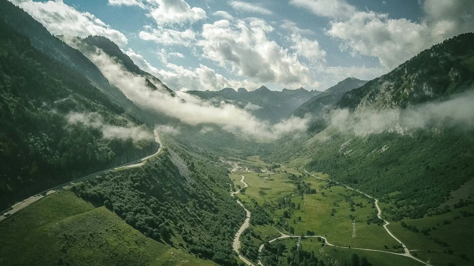 A green alpine valley under clouds, a road winding along the river