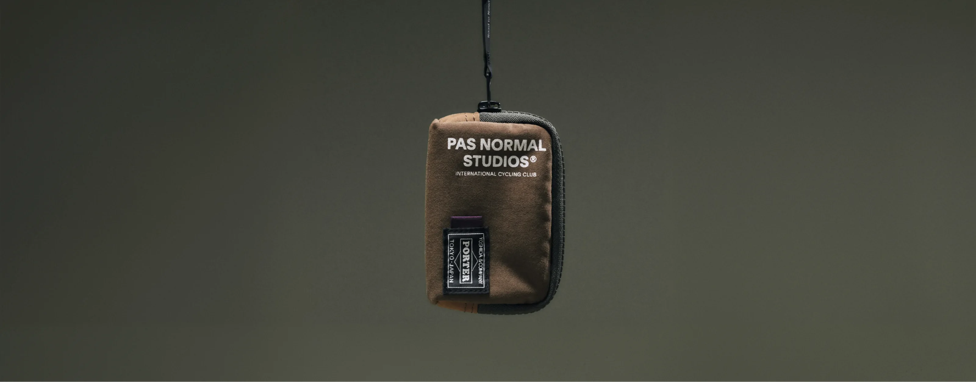 Brown Pas Normal Studios × PORTER pouch suspended from its strap